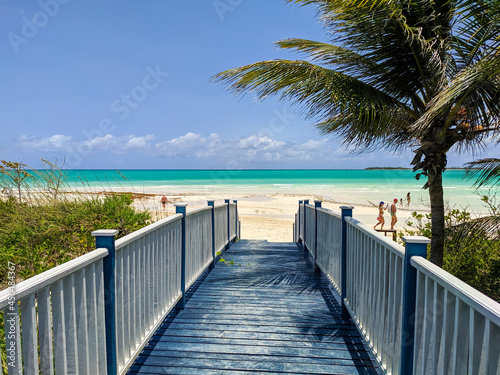 Cayo Guillermo, Cuba, 16 may 2021: Nice view from the wooden bridge to the Pilar beach. People relax, swim and walk along the white sand beach and azure ocean against the backdrop of the blue sky.