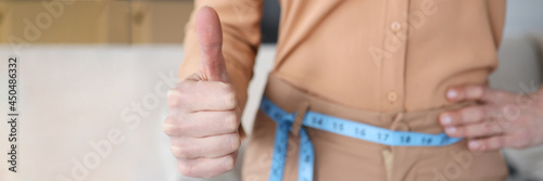 Woman with measuring tape at her waist showing thumb up closeup