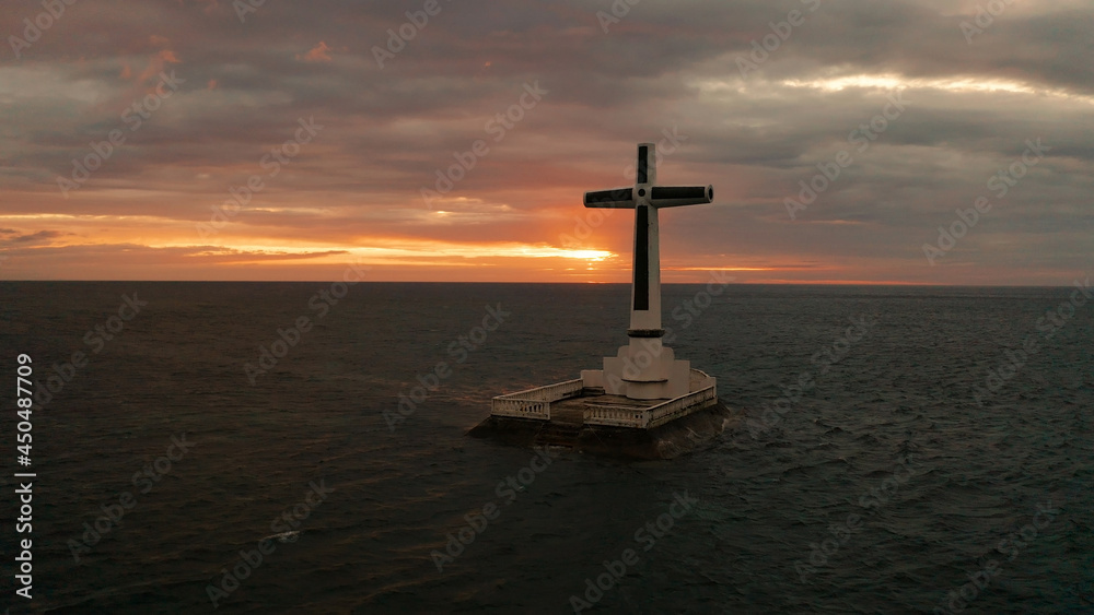Catholic cross in sunken cemetery in the sea at sunset, aerial drone. colorful sky during the sunset. Large crucafix marking the underwater sunken cemetary, Camiguin Island Philippines. Catholic cross in sunken cemetery in the sea at sunset, aerial drone. colorful sky during the sunset. Large crucafix marking the underwater sunken cemetary, Camiguin Island Philippines.