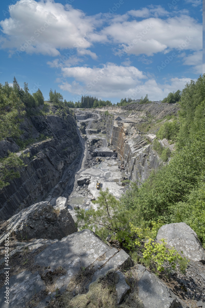 Under a blue sky is a view of a deep rock quarry where granite rocks ...