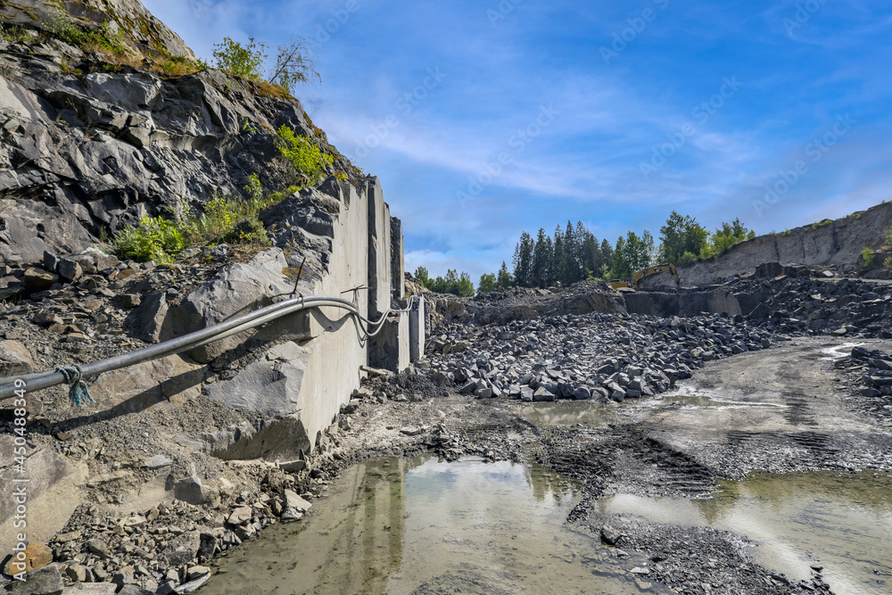 Under a blue sky is a view of a deep rock quarry where granite rocks