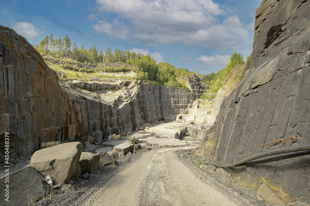Under a blue sky is a view of a deep rock quarry where granite rocks