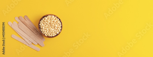 Hair removal film wax and wooden spatulas on yellow background. Depilation, beauty treatment. Banner 16:6. 