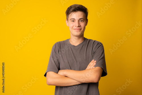 portrait of confident young man wearing casual t-shirt while standing on yellow background with arms folded