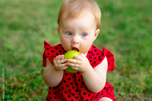 a baby eats a green apple in a red bodysuit on the green grass in summer, space for text