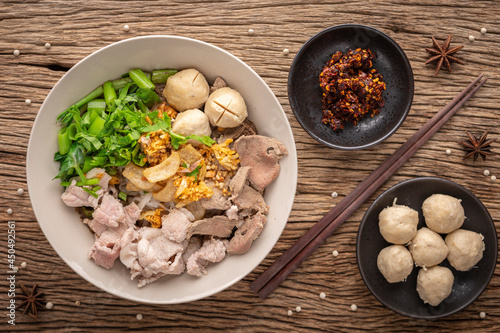 Guay Teaw, Guay Teow, Guay Tiew, Kuay Teow Neua, Thai food, noodle soup with beef, meatball, crackling, fried garlic, morning glory, chili, herb, pepper on rustic wood texture background, top view photo