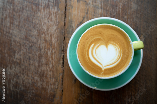 Top view of Latte coffee or cappuccino coffee in yellow cup with heart latte art on wooden table.