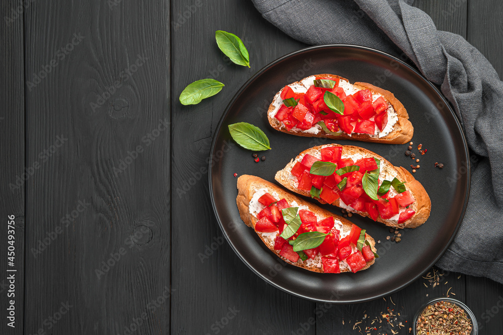 Bruschetta with tomato, butter, basil and cheese on a black background.