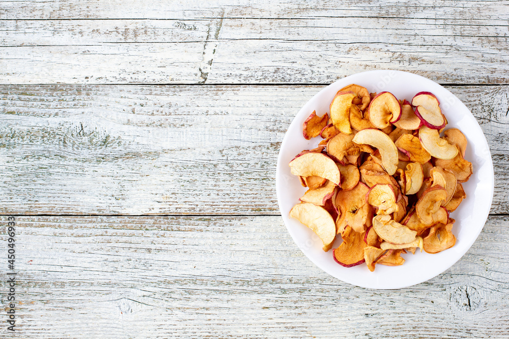 A pile of dried apples in slices on a white plate on wooden background. Dried fruit chips. Healthy food A pile of dried apples in slices on a white plate on wooden background. Dried fruit chips. Healthy food