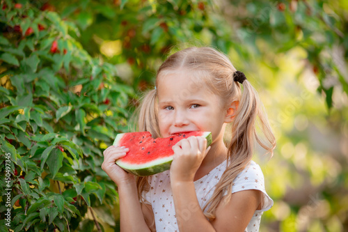 a little girl holds a piece of watermelon in the summer sun