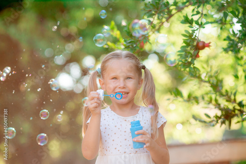 a little girl blows soap bubbles in the park