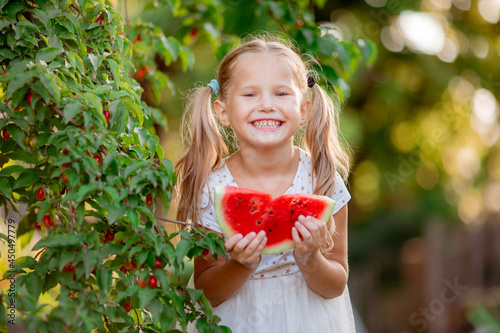 a little girl holds a piece of watermelon in the summer sun