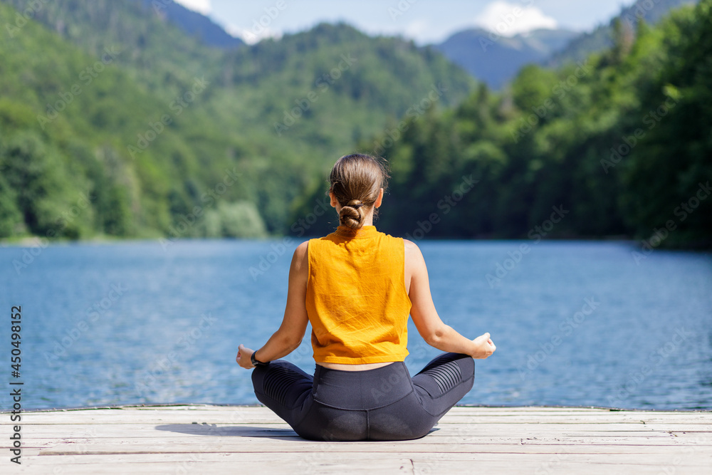 Young woman meditating or practicing yoga at the lake in the mountains.