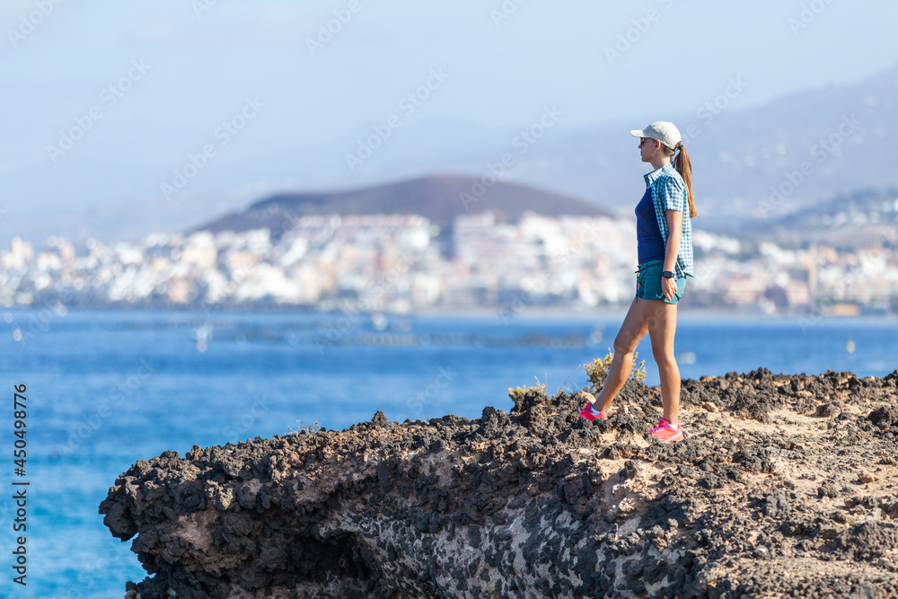 Young slim woman in shorts and top enjoying summer vacation near ocean. Sporty woman looking at the ocean standing at the coast