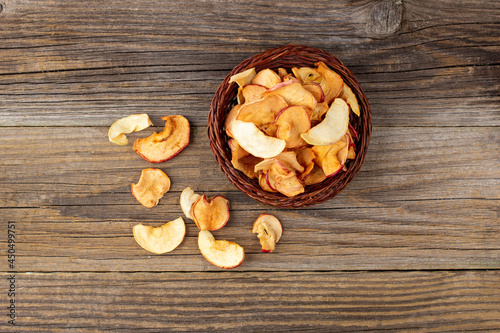 A pile of dried slices of apples in wicker basket on wooden background. Dried fruit chips. Healthy food