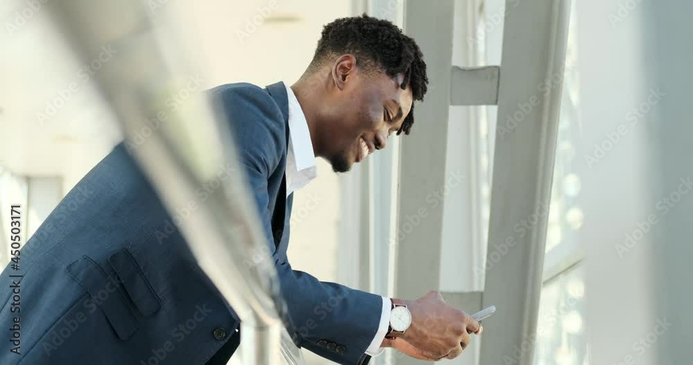 African american businessman text messaging using mobile phone while leaning on fence at airport African american businessman text messaging using mobile phone while leaning on fence at airport