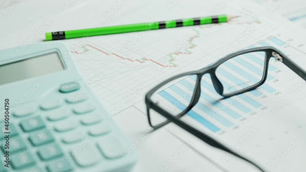 Documents with calculator. Printed stock graphs and charts. Analyzing financial data report and business concept. Profit and tables on work desk Documents with calculator. Printed stock graphs and charts. Analyzing financial data report and business concept. Profit and tables on work desk