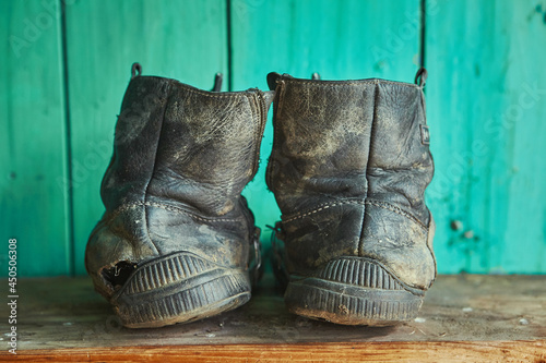 Old dirty torn shoes stand on a wooden shelf against the background of a green wall.