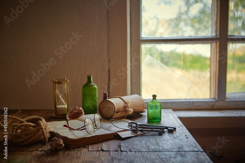 On the old table are: an old book, manuscripts, bottles for potions and poisons, a seashell, a magnifying glass in a brass frame, an old pince-nez, rusty keys to chests, a sea rope