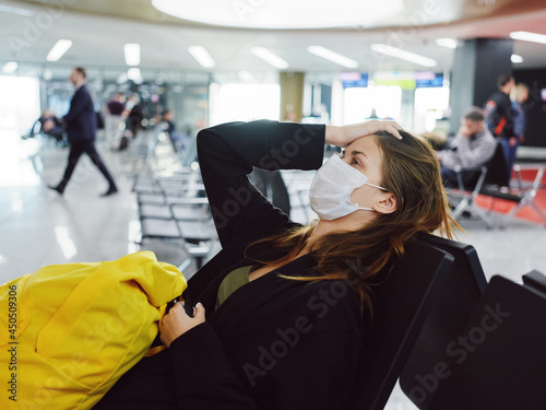 woman holding her head in medical mask airport passenger waiting for flight