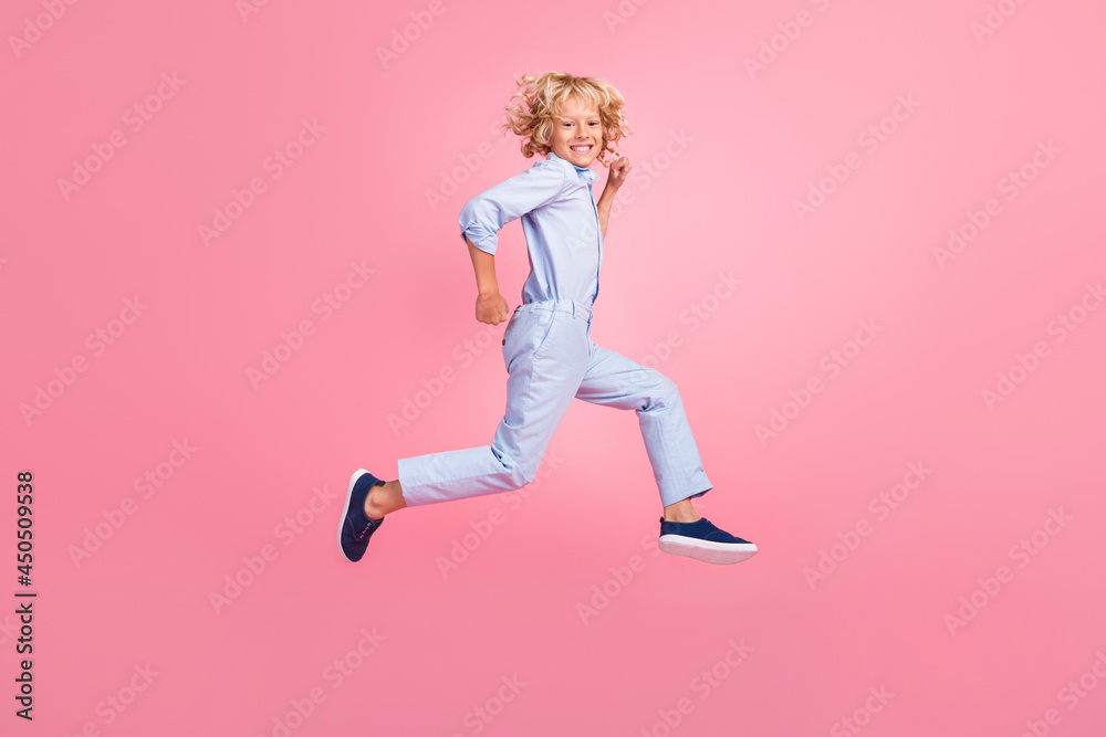 Full size profile side photo of smiling boy running fast speed in air freedom summer isolated on pink color background Full size profile side photo of smiling boy running fast speed in air freedom summer isolated on pink color background