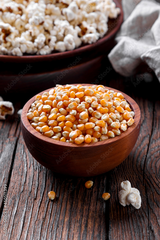 grains of popcorn on a dark background, in a wooden bowl, on the background ready popcorn, rustic