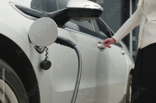 Business woman opens or closes the door of an electric car. Eco friendly alternative energy green environment concept