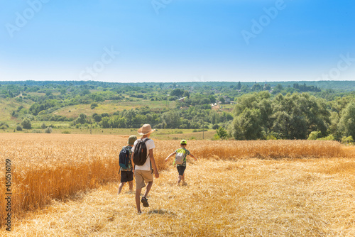 Three young boys with backpacks go hiking along the wheat field.