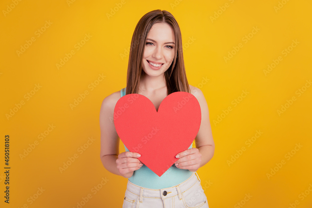 Portrait of adorable romantic lady hold demonstrate red paper heart card on yellow background Portrait of adorable romantic lady hold demonstrate red paper heart card on yellow background
