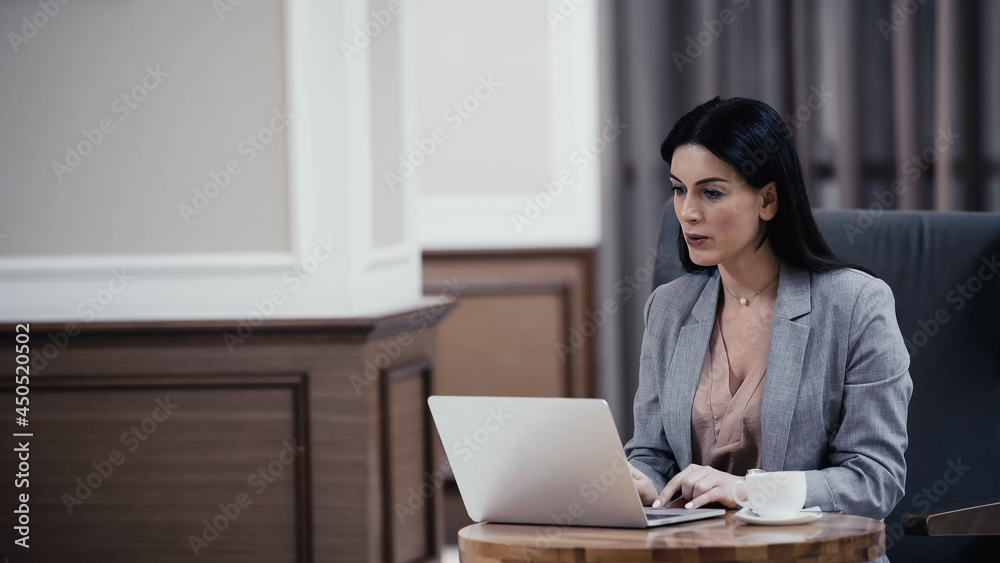 businesswoman having video call on laptop near cup of coffee on table in lobby of restaurant businesswoman having video call on laptop near cup of coffee on table in lobby of restaurant