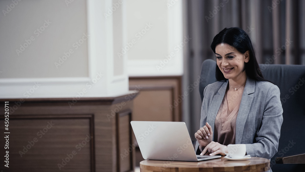 happy businesswoman having video call on laptop near cup of coffee on table in lobby of restaurant happy businesswoman having video call on laptop near cup of coffee on table in lobby of restaurant