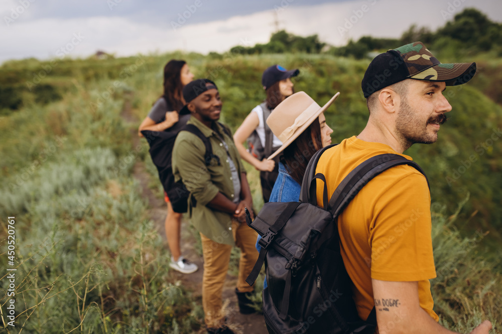 Group of friends, young men and women walking, strolling together outskirts of city, in summer forest, meadow. Active lifestyle, friendship, care, ecology concept