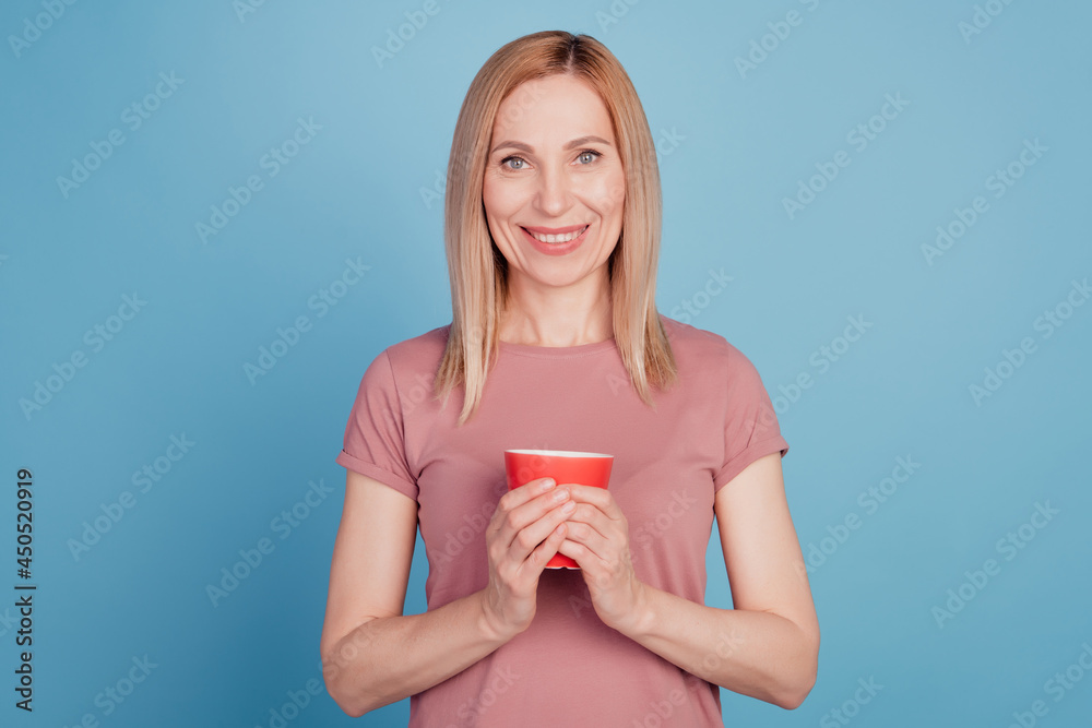 Photo of cheerful positive woman holding mug of coffee smiling toothily isolated over blue color background Photo of cheerful positive woman holding mug of coffee smiling toothily isolated over blue color background