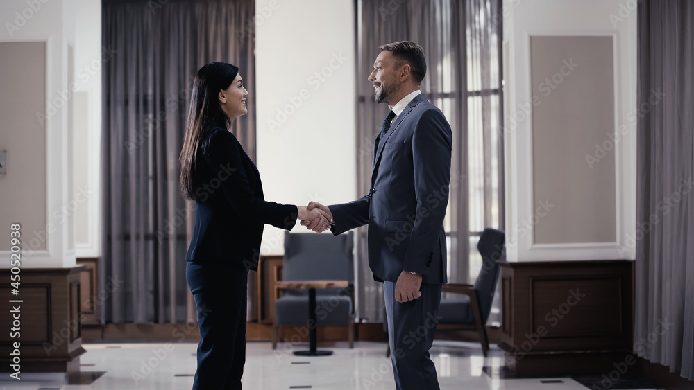 side view of smiling businesswoman shaking hands with businessman in lobby of restaurant side view of smiling businesswoman shaking hands with businessman in lobby of restaurant