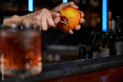 Fotografia bartender makes a cocktail in a glass with orange peel