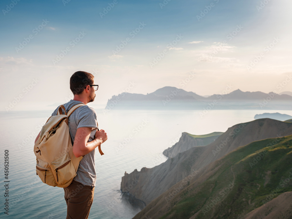 Young man travels alone on the backdrop of the mountains, the lifestyle concept of traveling outdoors. Looking at distance with the blue sea in front.