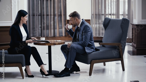 Businessman drinking coffee during business meeting with woman in restaurant lobby