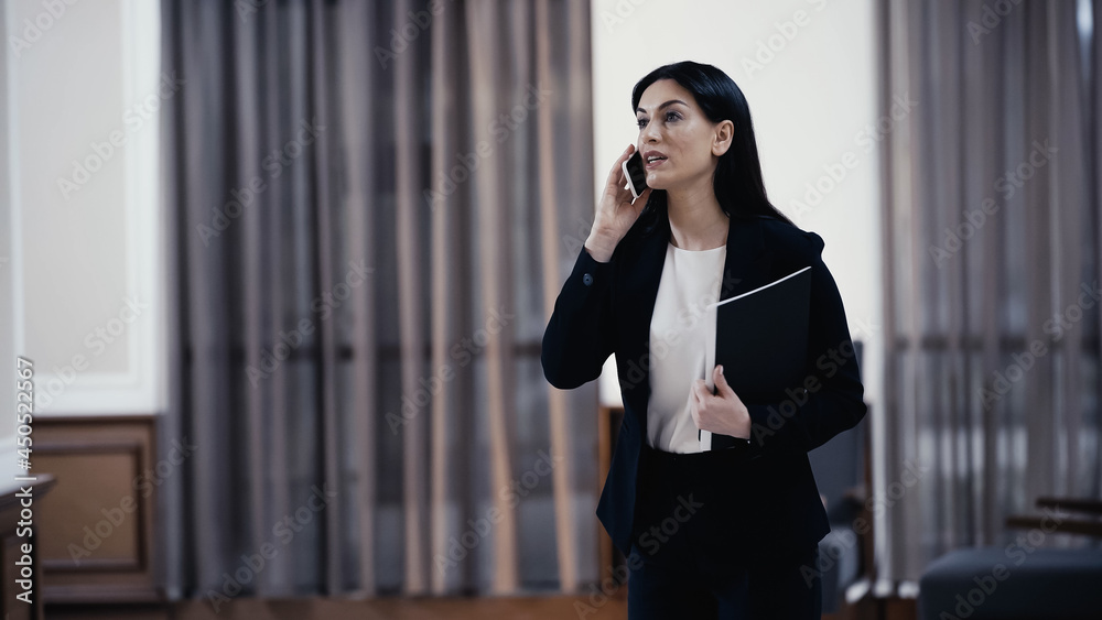 Businesswoman with paper folder talking on smartphone in lobby of restaurant Businesswoman with paper folder talking on smartphone in lobby of restaurant