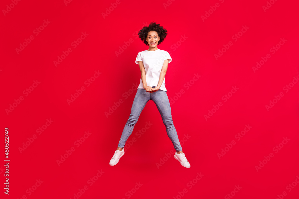 Full length body size photo smiling curly woman jumping up happy isolated vivid red color background Full length body size photo smiling curly woman jumping up happy isolated vivid red color background