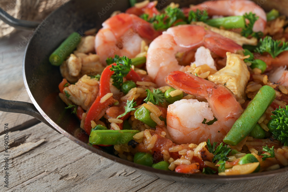 Rice dish with seafood, chicken and vegetables in a paella pan on a rustic wooden table, close up, selected focus Rice dish with seafood, chicken and vegetables in a paella pan on a rustic wooden table, close up, selected focus