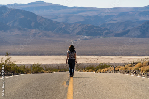 Female walking on the asphalt road looking at mountains in the USA - death valley