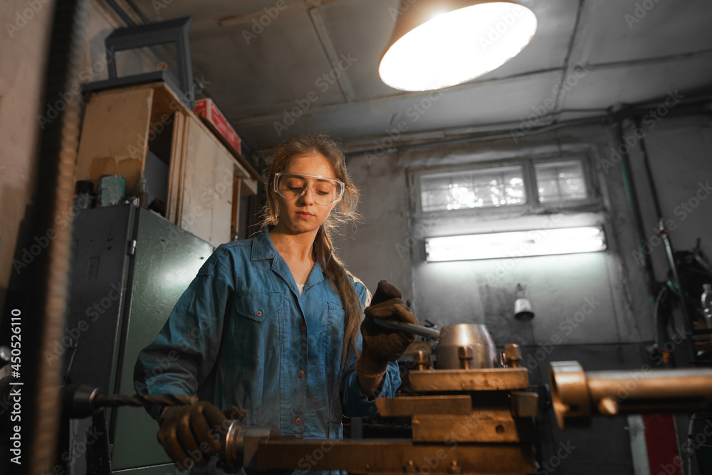 young woman in her garage works on a lathe. Profession concept Turner, Metalworking, Turning, Industry, Metal.