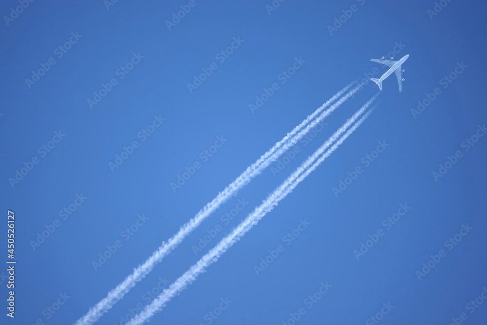 Large four engine passenger supersonic airplane flying from left to right high in blue cloudless sky leaving long white tracks Large four engine passenger supersonic airplane flying from left to right high in blue cloudless sky leaving long white tracks
