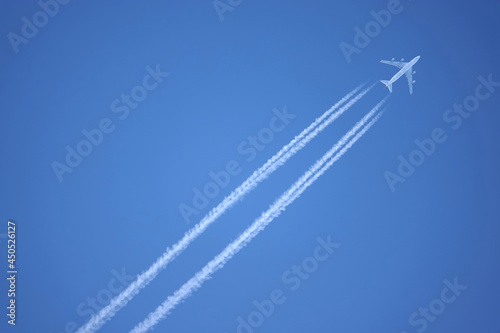 Large four engine passenger supersonic airplane flying from left to right high in blue cloudless sky leaving long white tracks photo