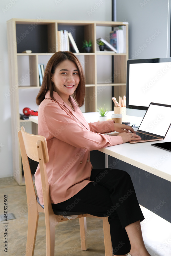 Portrait with businesswoman in pastel suit sitting in front of laptop and computer, empty screen of notebook and PC, Business and financial concept. Portrait with businesswoman in pastel suit sitting in front of laptop and computer, empty screen of notebook and PC, Business and financial concept.