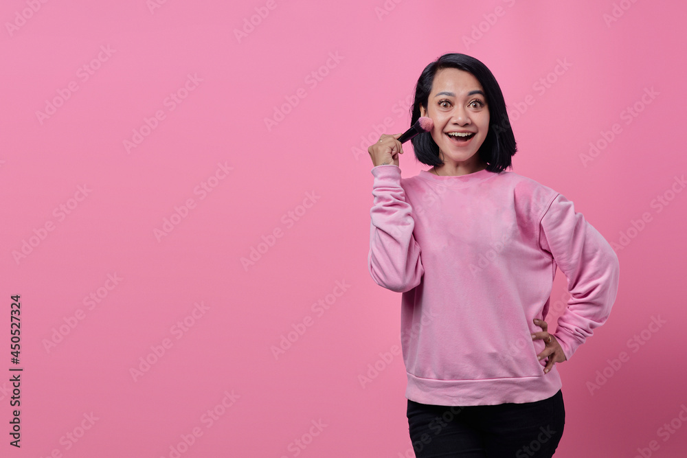 Portrait of smiling Asian woman with makeup brush in hands on pink background Portrait of smiling Asian woman with makeup brush in hands on pink background