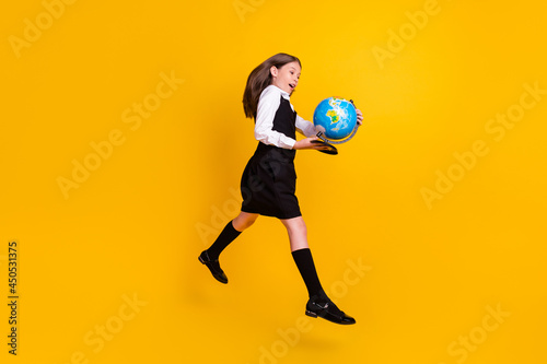 Full length photo of brunette girl knowledge go hold globe jump up wear uniform isolated on yellow color background © deagreez