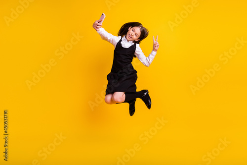 Full length body size photo schoolgirl jumping taking selfie showing v-sign isolated vivid yellow color background