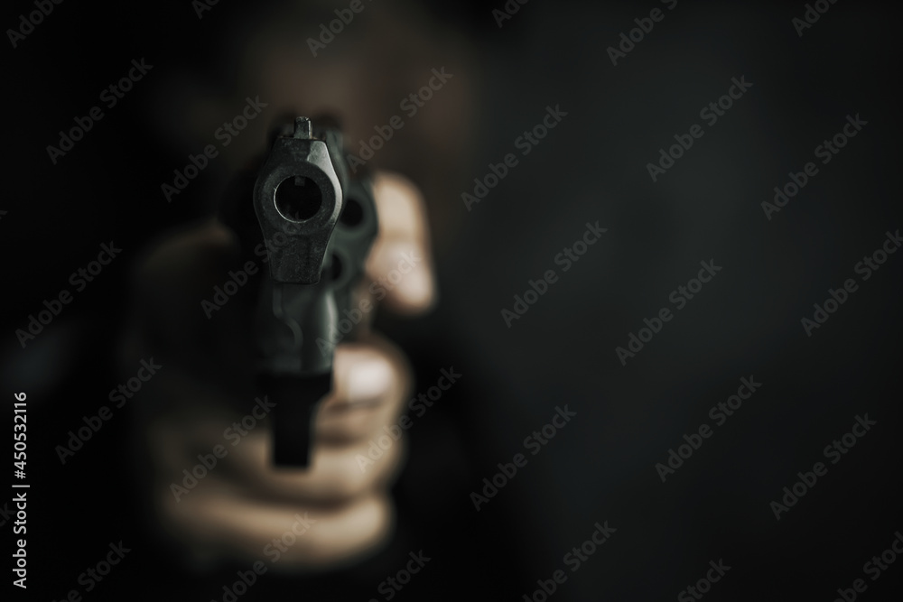 Threat of firearms. Muzzle of gun in man's hand is pointed at camera. Male criminal holds revolver on black background. Attack or defense. Threat of firearms. Muzzle of gun in man's hand is pointed at camera. Male criminal holds revolver on black background. Attack or defense.