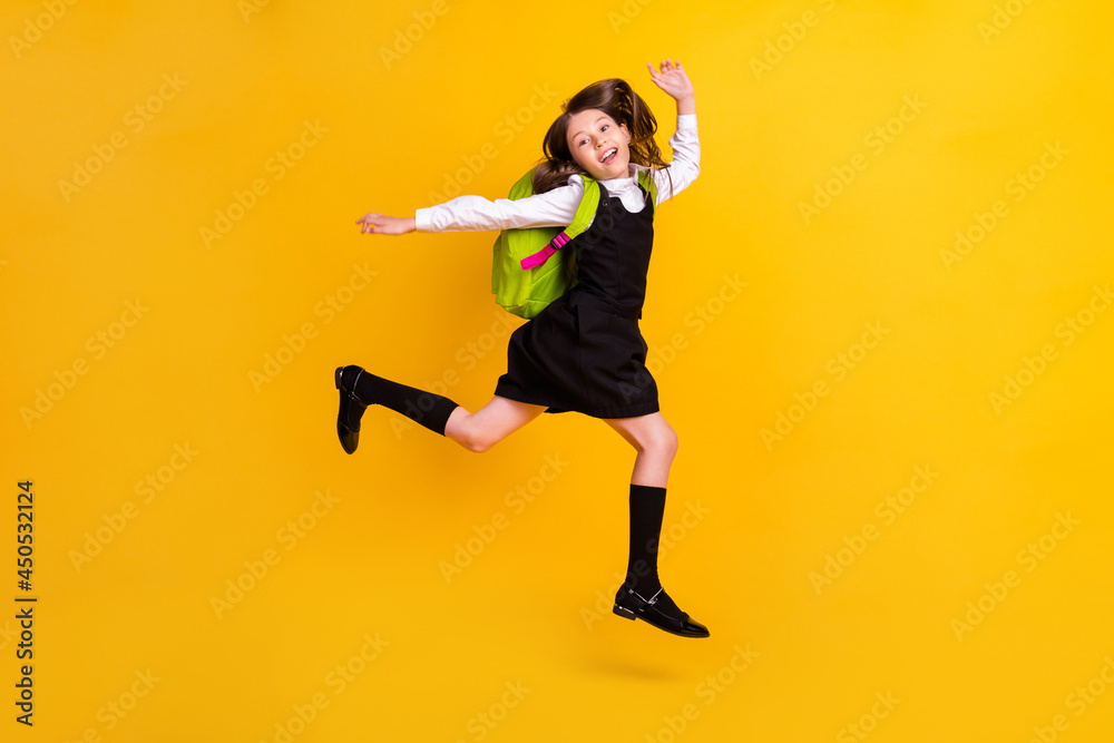 Full length photo of cheerful happy amazed small girl jump up wear backpack isolated on yellow color background